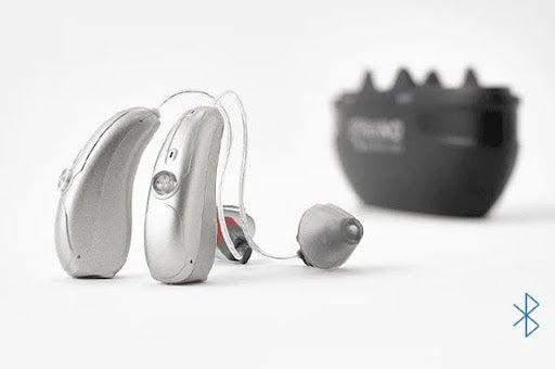 A pair of Nano hearing aids next to a black charging case.