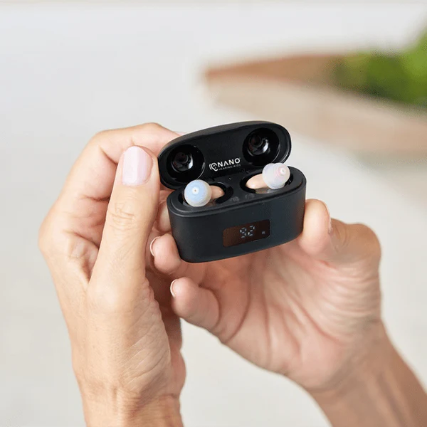 A person holding Nano hearing aids in a charging case.