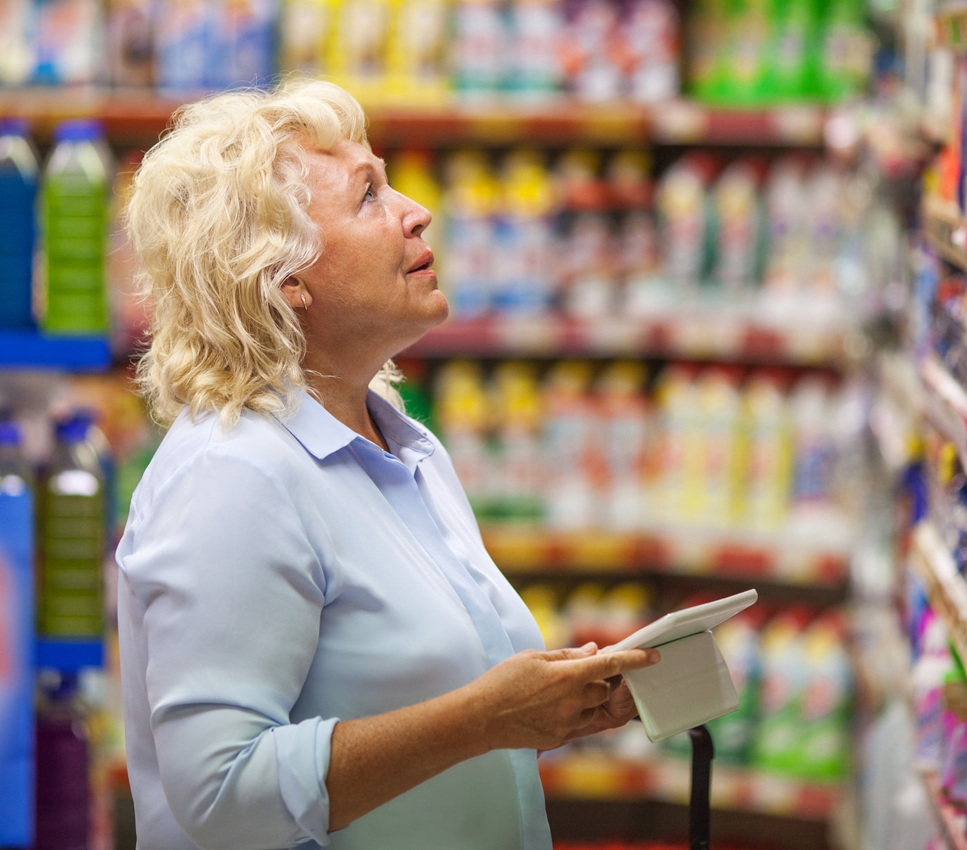 An older woman checking out products in a supermarket aisle.