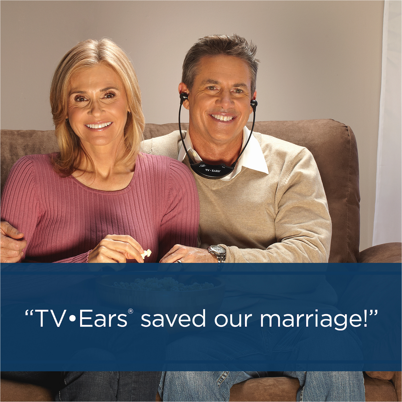 A couple sitting and watching television with the man using TV Ears.